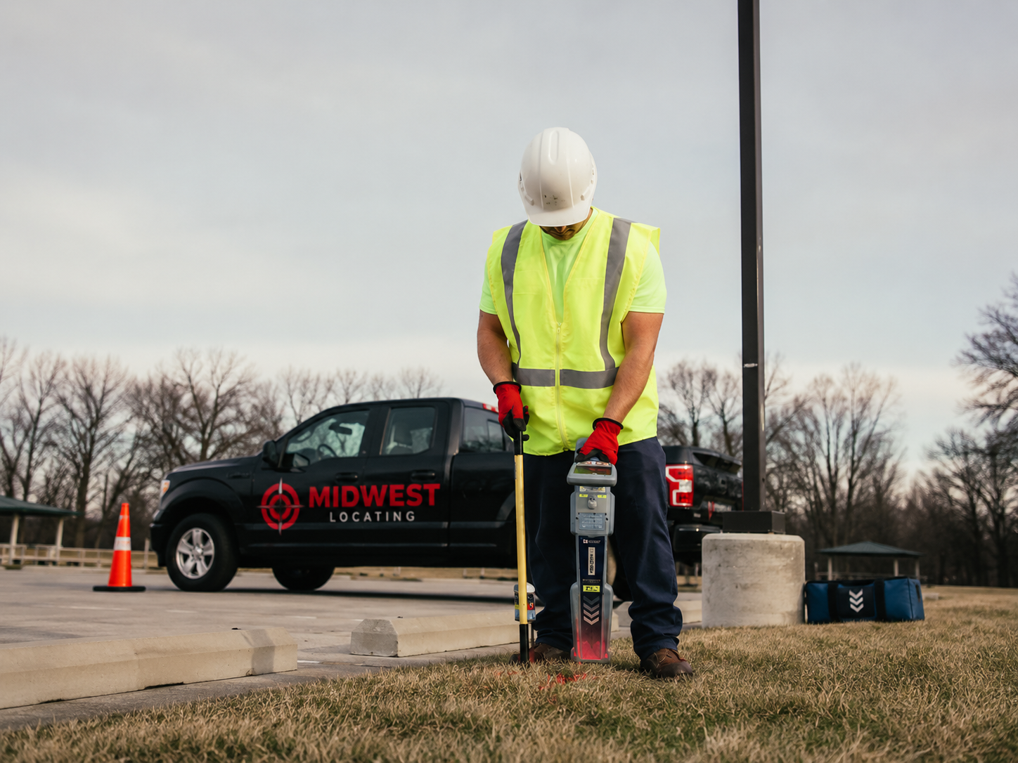 Midwest Locating technician using electromagnetic locator next to branded truck